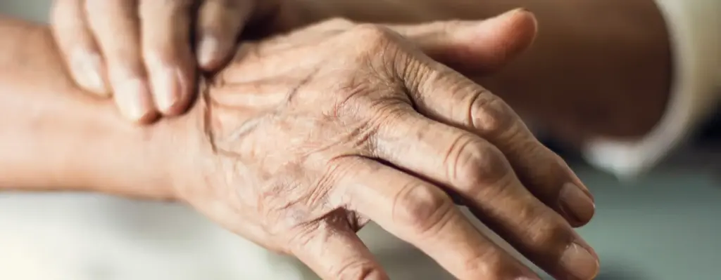 Das Bild zeigt eine ältere Hand einer Person. Die Person greift sich mit der anderen Hand ans Handgelenk. Das Bild wird im Bereich "ParkinsonGo – digitale Therapiehilfe" verwendet.