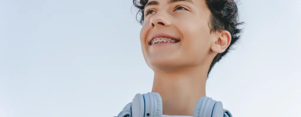 Ein Teenager blickt in die Ferne. Er lächelt und trägt eine Zahnspange. Das Bild wird im Bereich "Retentionsspange" verwendet.