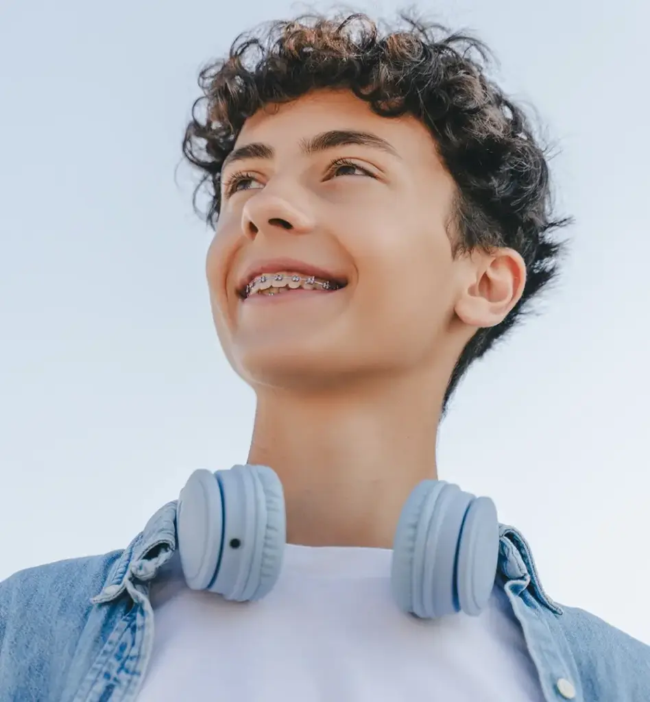 Ein Teenager blickt in die Ferne. Er lächelt und trägt eine Zahnspange. Das Bild wird im Bereich "Retentionsspange" verwendet.