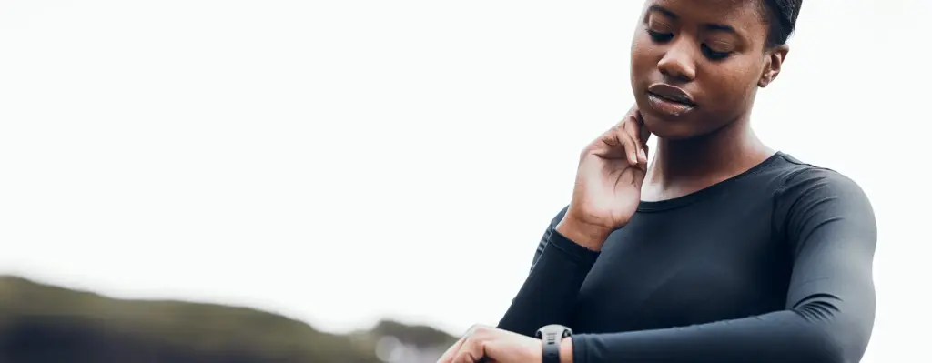 Das Bild zeigt eine Frauim Sportoutfit. Sie fühlt ihren Puls am Hals und schaut dabei auf ihre Sportuhr. Das Bild wird im Bereich "Sportmedizinische Untersuchung: Leistung & Sicherheit steigern" verwendet.