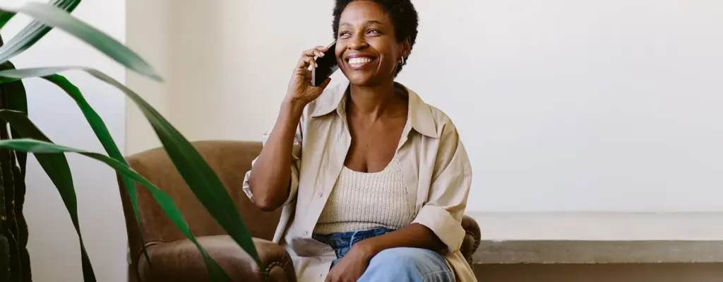 Das Bild zeigt eine Frau, die auf einem Sessel sitzt. Sie telefoniert mit einem Smartphone. Neben ihr steht eine Pflanze. Das Bild wird im Bereich "Telefoncoaching – Wir sind immer an Ihrer Seite!" verwendet.