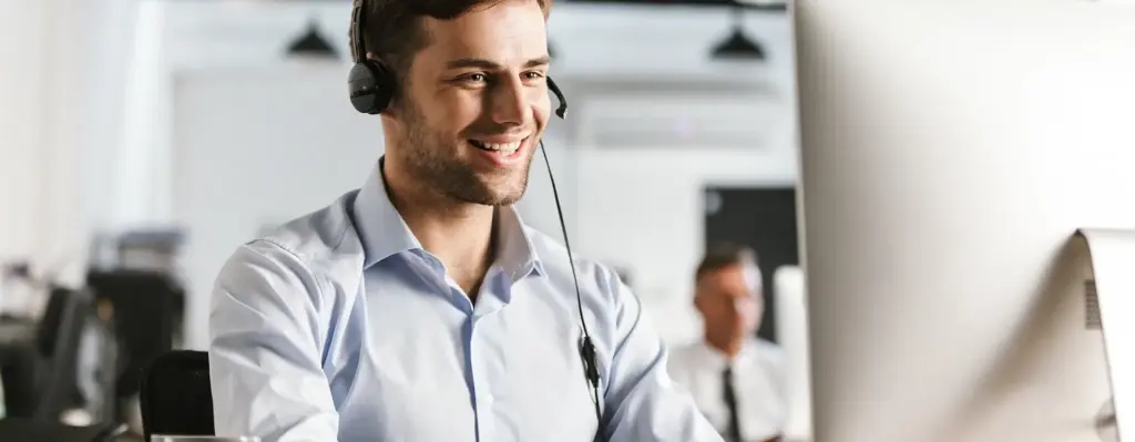 Das Bild zeigt einen jungen Mann mit Hemd, der ein Headset trägt und an einem PC sitzt. Das Bild wird im Bereich "Terminservicestellen" verwendet.