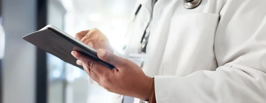 Das Bild zeigt einen Arzt im weißen Kittel mit einem Tablet in der Hand. Er tippt etwas auf den Bildschirm. Der Arzt ist dabei nur vom Brustkorb bis zum Bauch zu sehen. Das Bild wird im Bereich "Versorgung von Patienten mit Herzinsuffizienz (CorBene)" verwendet.