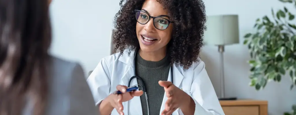 Das Bild zeigte eine Frau mit Brille. Sie ist Ärztin und erklärt ihrer Patientin vor sich etwas. Das Bild wird im Bereich "Versorgungsprogramme" verwendet.