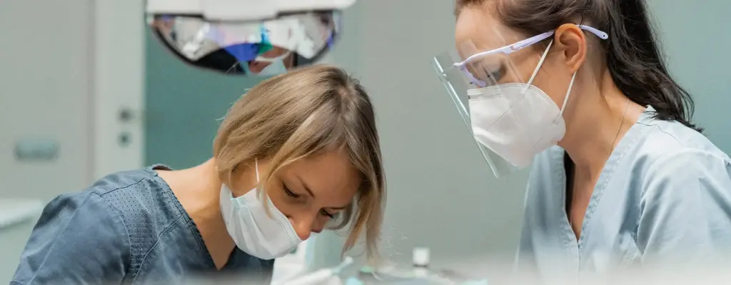 Das Bild zeigt zwei beim Zahnarzt arbeitende Personen während einer Behandlung. Sie tragen Schutzmasken und eine von ihnen auch eine Schutzbrille. Das Bild wird im Bereich "Vollnarkose und Lachgas-Sedierung bei Entfernung der Weisheitszähne" verwendet.