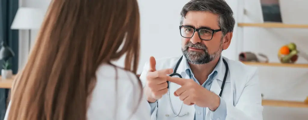 Das Bild zeigt einen Arzt, der an einem Tisch sitzt, gestikuliert und einer Frau etwas erklärt. Die Frau ist nur mit dem Rücken zu sehen. Das Bild wird im Bereich "Zweitmeinung bei Krebsdiagnosen" verwendet.