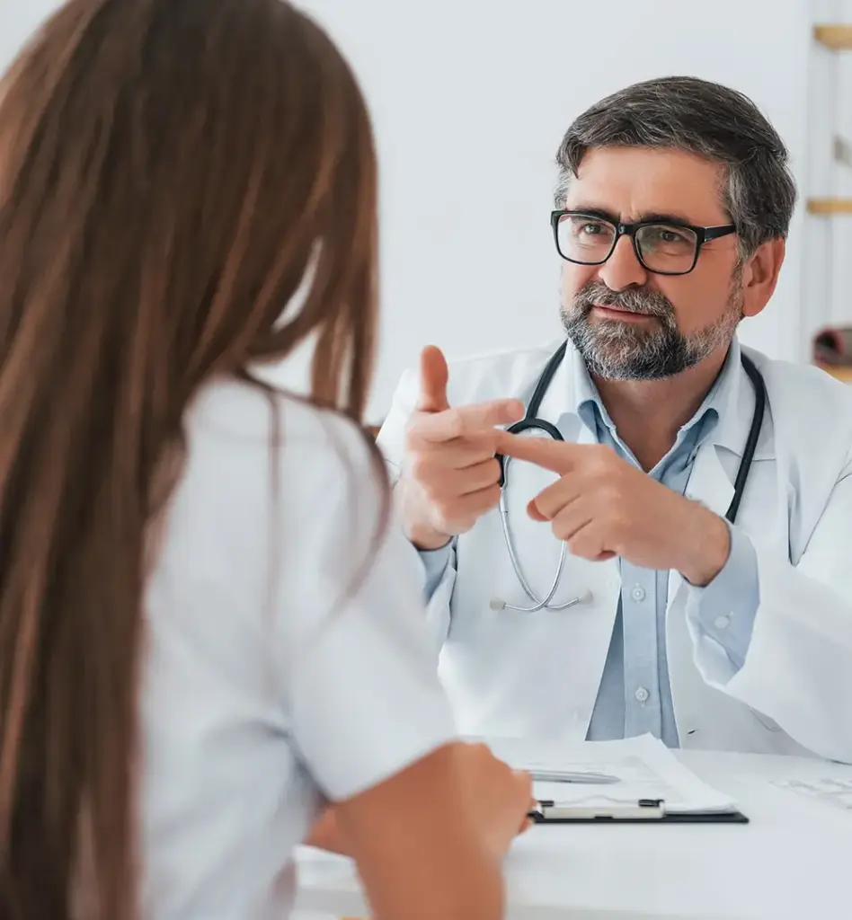 Das Bild zeigt einen Arzt, der an einem Tisch sitzt, gestikuliert und einer Frau etwas erklärt. Die Frau ist nur mit dem Rücken zu sehen. Das Bild wird im Bereich "Zweitmeinung bei Krebsdiagnosen" verwendet.