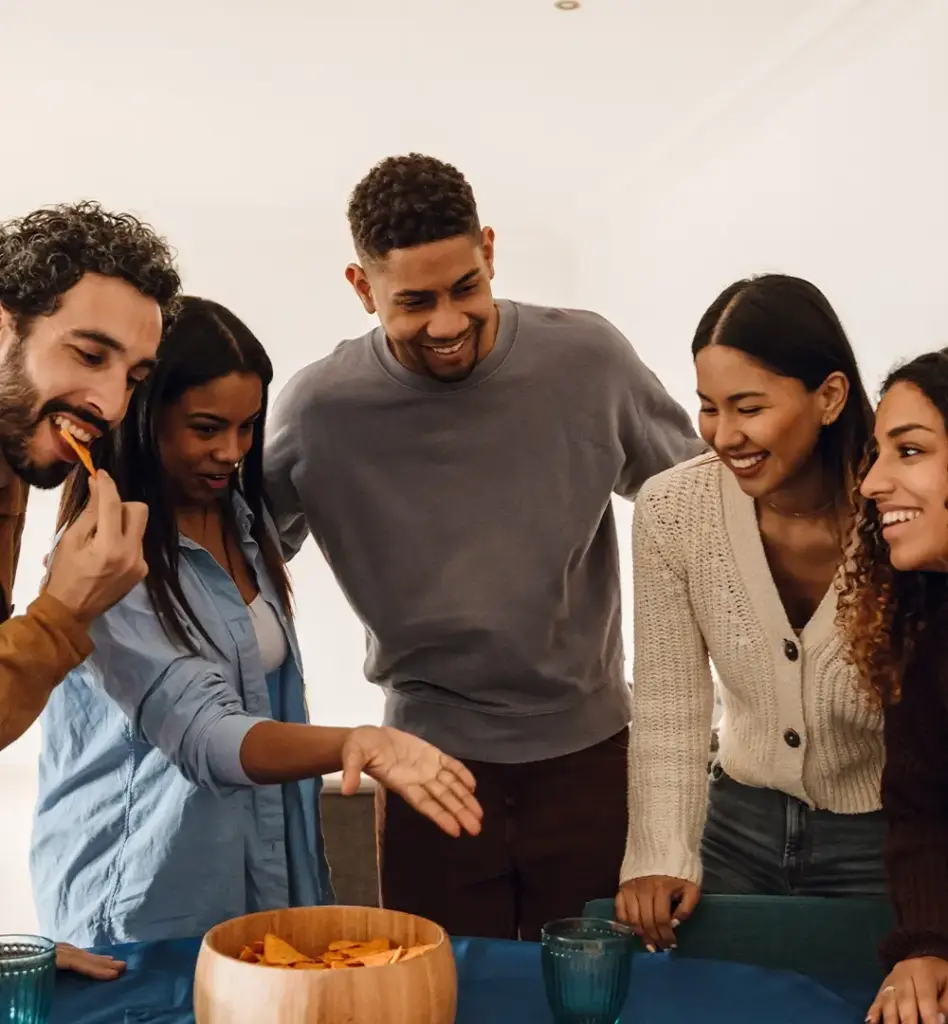 Mehrere junge Menschen stehen zusammen um einen Tisch herum. Sie lachen.