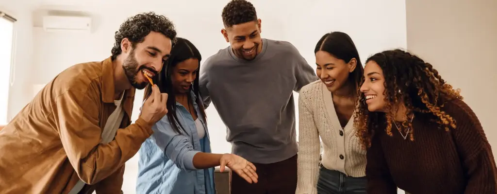 Mehrere junge Menschen stehen zusammen um einen Tisch herum. Sie lachen.