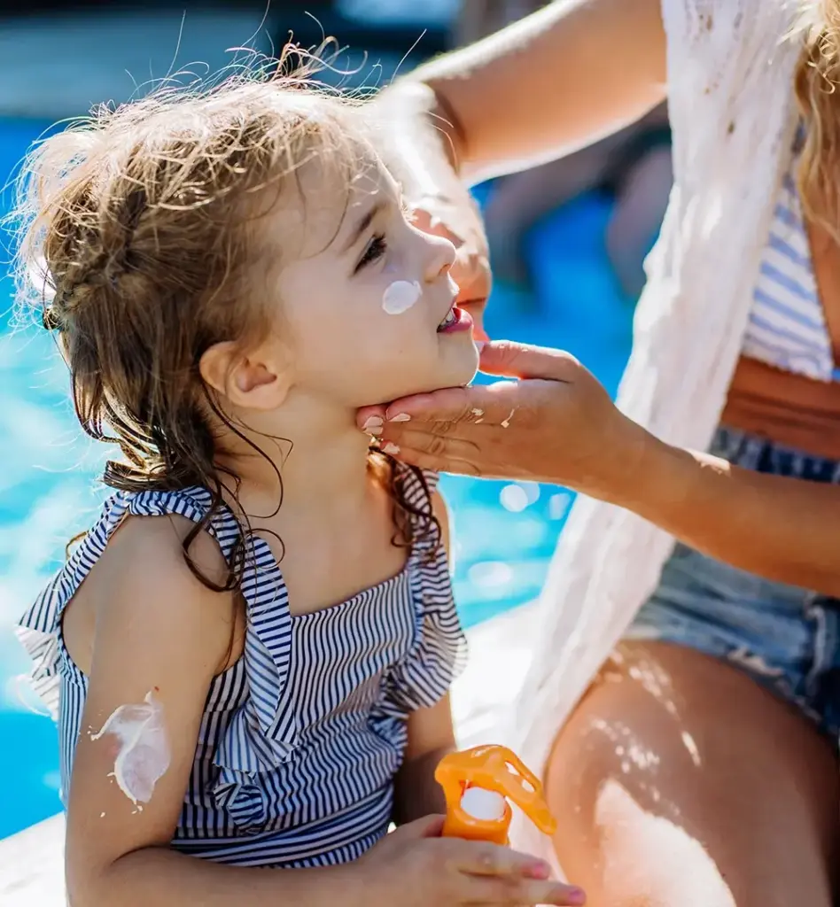 Eine Frau cremt ein kleines Mädchen im Gesicht mit Sonnencreme ein.