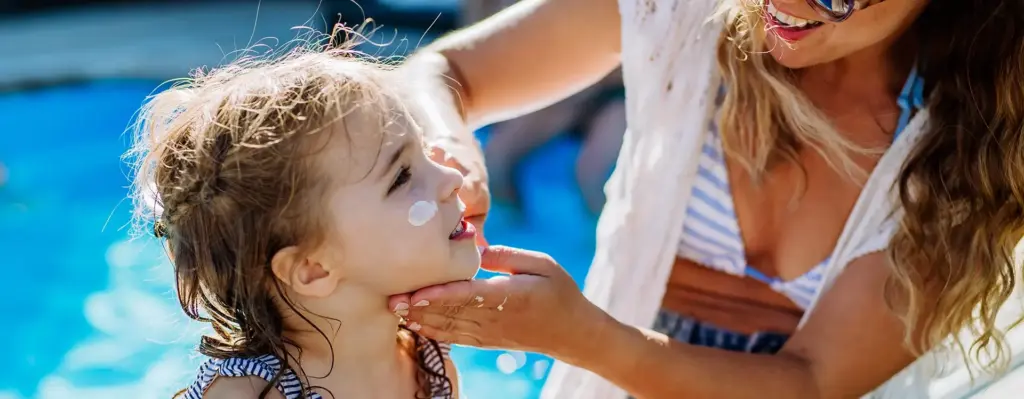 Eine Frau cremt ein kleines Mädchen im Gesicht mit Sonnencreme ein.