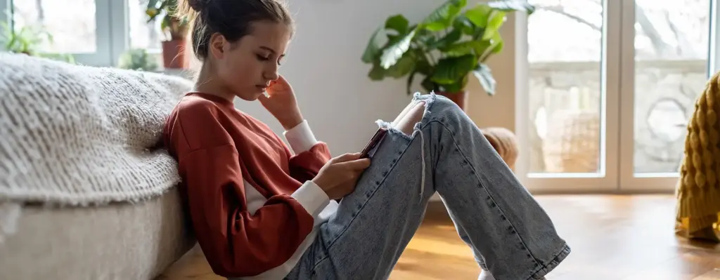 Ein Mädchen sitzt auf dem Boden und schaut traurig auf ihr Handy.