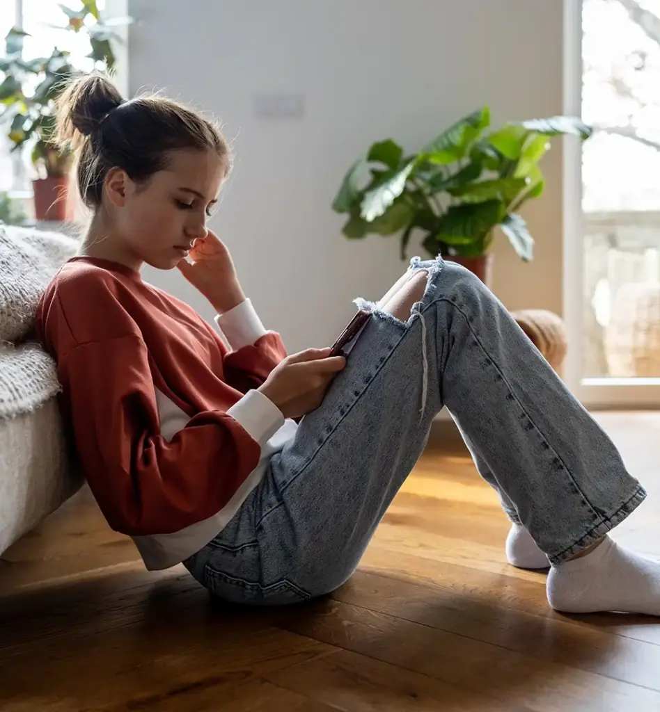 Ein Mädchen sitzt auf dem Boden und schaut traurig auf ihr Handy.