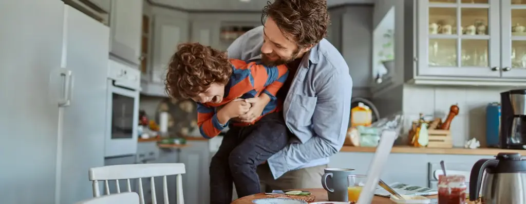Ein Mann hält einen Jungen auf dem Arm und sie lachen und scheinen sich zu kabbeln.