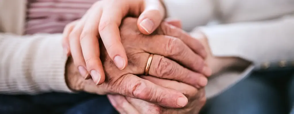 Man sieht Hände einer älteren Person mit einem Ehering. Eine Hand einer jüngeren Person liegt auf den Händen der älteren Person. Das Bild wird im Bereich "Pflegegeld" verwendet.