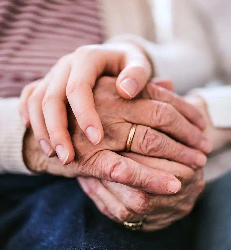 Man sieht Hände einer älteren Person mit einem Ehering. Eine Hand einer jüngeren Person liegt auf den Händen der älteren Person. Das Bild wird im Bereich "Pflegegeld" verwendet.