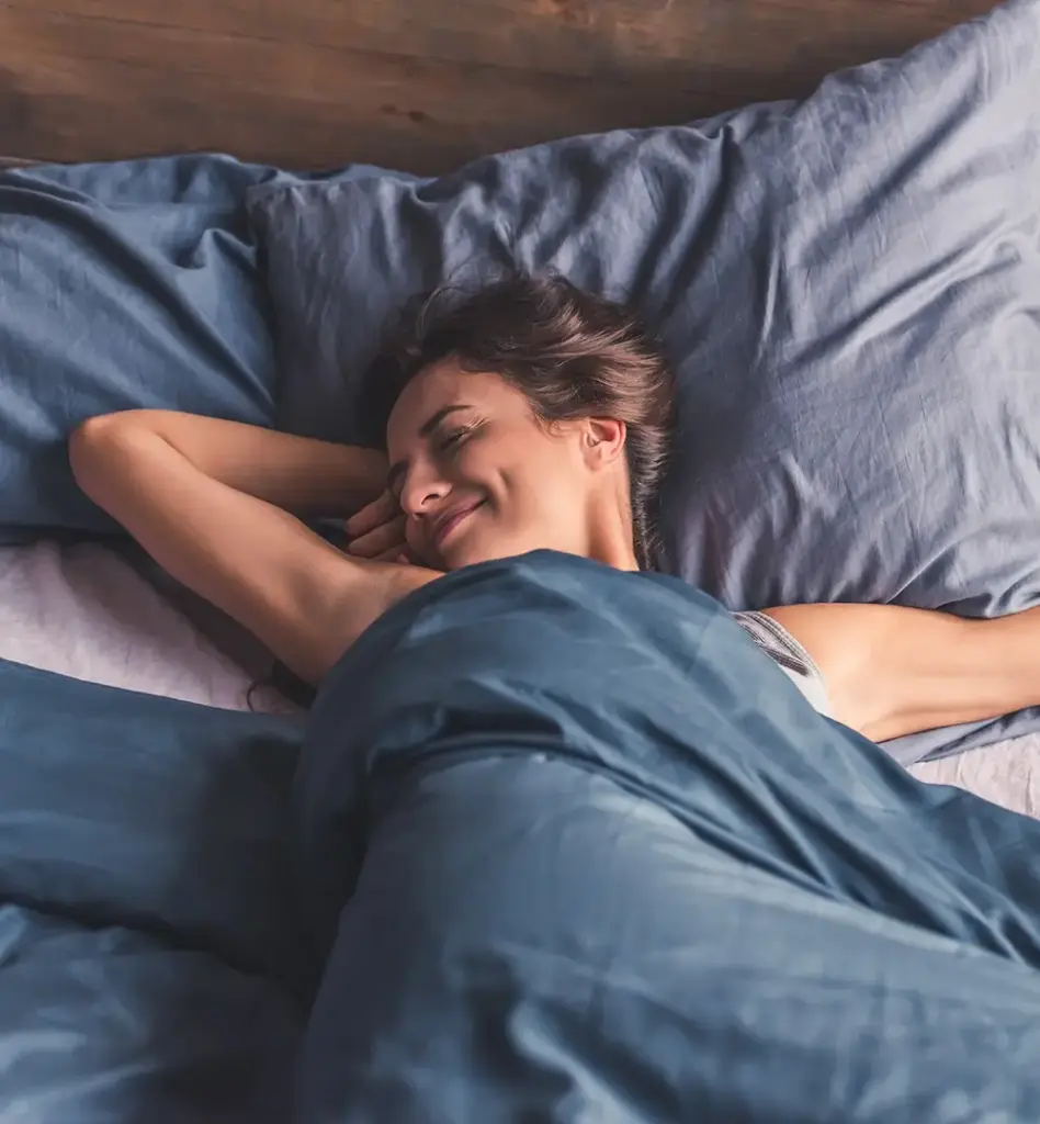 Eine Frau liegt entspannt im Bett, lächelt und streckt sich.
