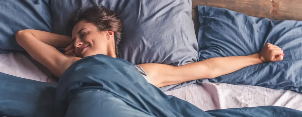 Eine Frau liegt entspannt im Bett, lächelt und streckt sich.