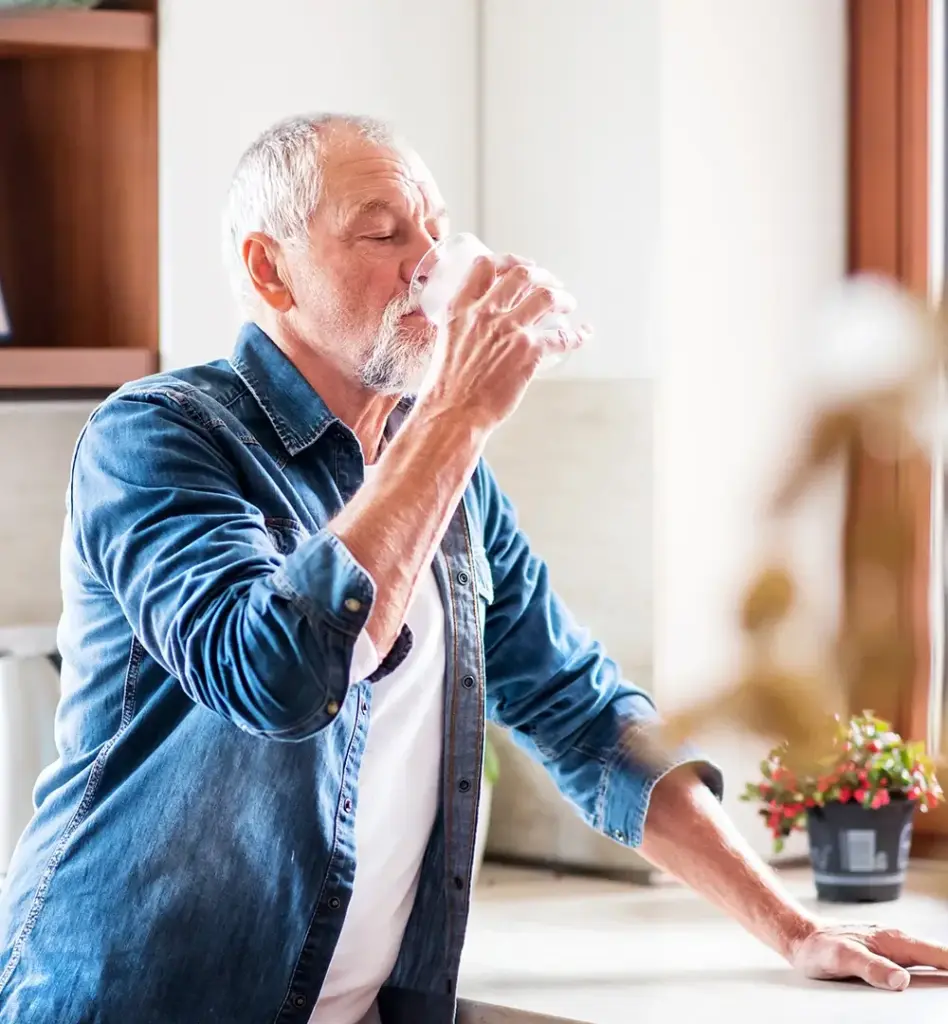 Ein Mann steht in der Küche und trinkt ein Glas Wasser.