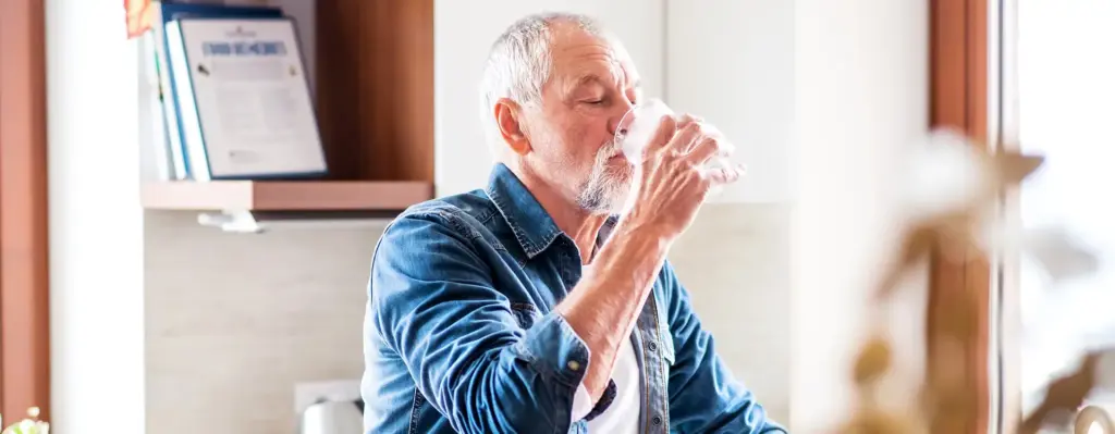 Ein Mann steht in der Küche und trinkt ein Glas Wasser.