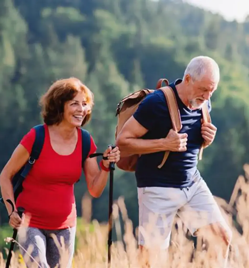Ein Paar geht mit Wanderstöcken und Rucksäcken in den Bergen über ein Feld spazieren.