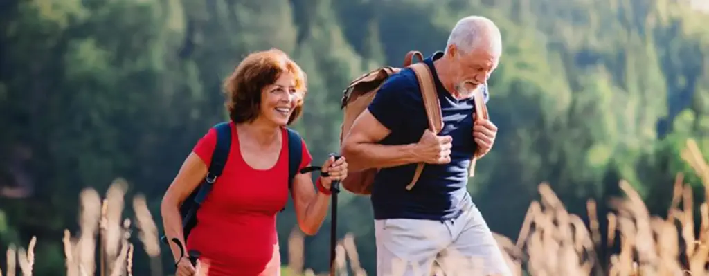 Ein Paar geht mit Wanderstöcken und Rucksäcken in den Bergen über ein Feld spazieren.