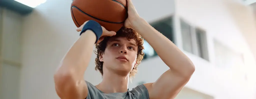 Ein junger Mann in Sportkleidung hält einen Basketball mit beiden Händen hoch und setzt zum Wurf an. Das Bild wird im Bereich "Aktivbonus Präventionskurs" verwendet.