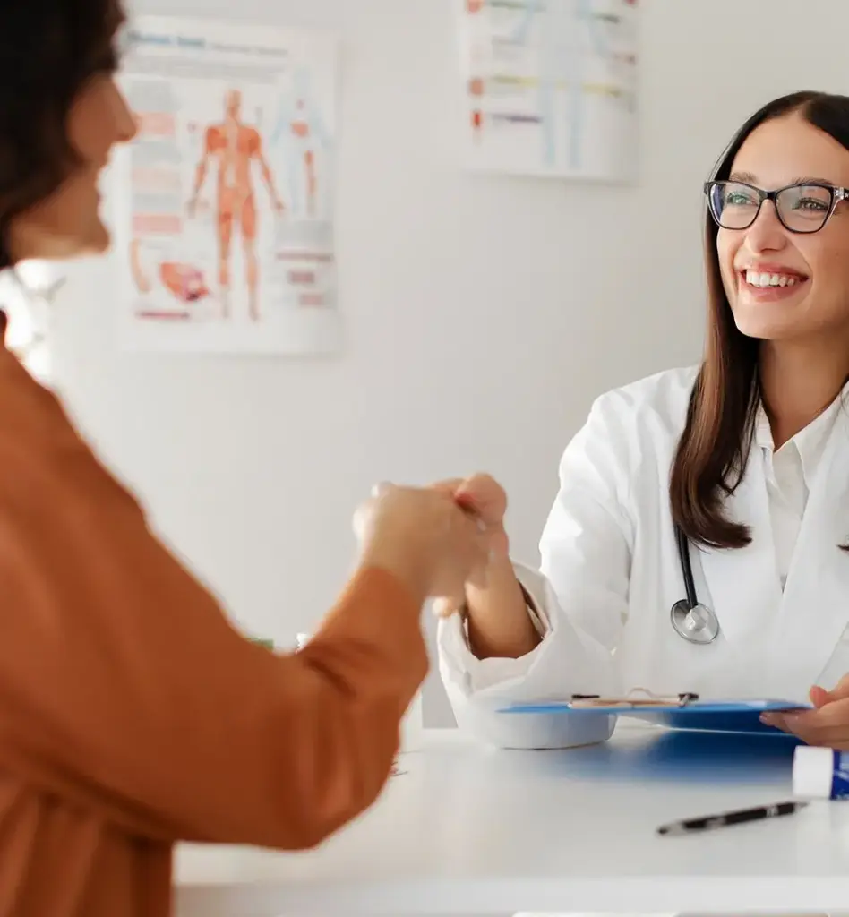 Das Bild zeigt eine Ärztin an ihrem Schreibtisch. Sie reicht einer Patientin im Bildvordergrund die Hand. Das Bild wird im Bereich "Gesundheitsuntersuchung Check Up" verwendet.