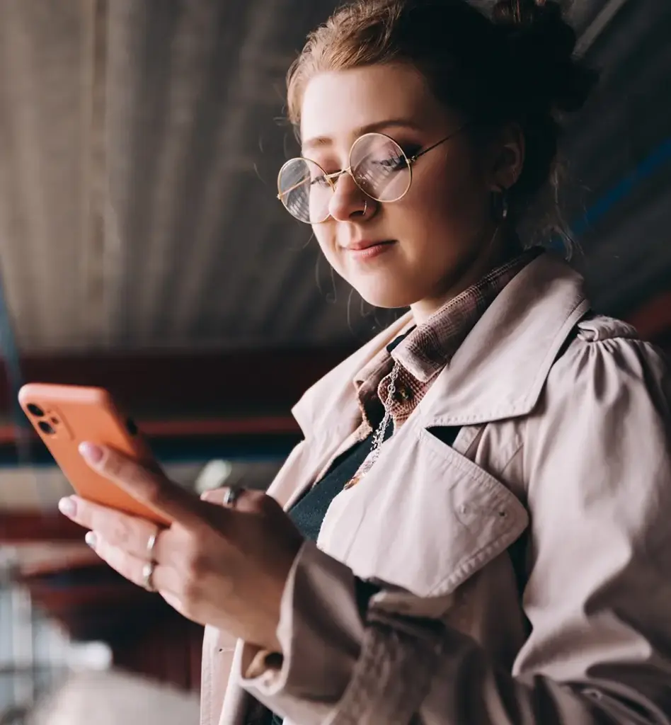 Das Bild zeigt eine jüngere Frau mit Brille und Nasenpiercing. Sie hält ein Smartphone in der Hand und blickt darauf. Das Bild wird im Bereich "Medizinischer Rat – wann und wo du ihn brauchst" verwendet.