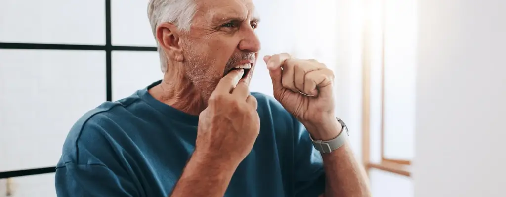 Das Bild zeigt einen älteren Mann, der Zahnseide benutzt. Er steht im Badezimmer. Das Bild wird im Bereich "Zahngesundheit: ein Leben lang gut versorgt" verwendet.