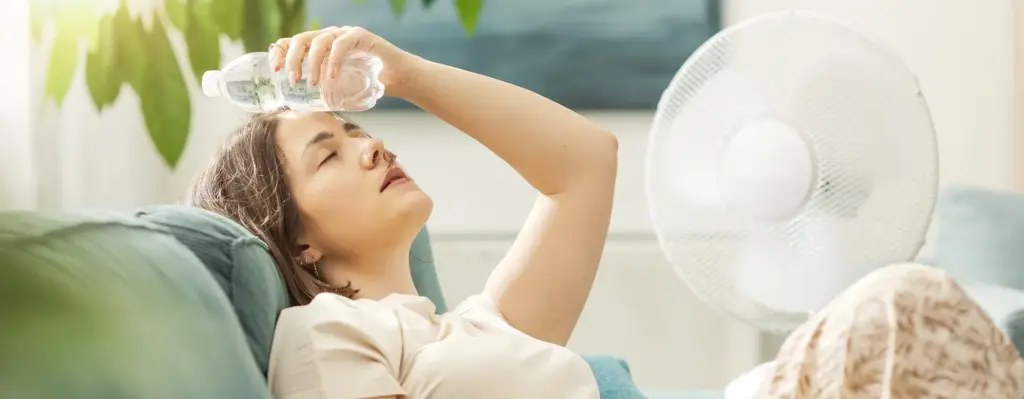 Eine Frau liegt auf dem Sofa und hält sich eine Wasserflasche zum Kühlen an die Stirn.