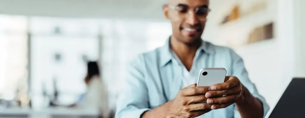 Das Bild zeigt einen Mann am Schreibtisch, der auf sein Smartphone blickt. Hand und Smartphone sind scharf, der Rest ist unscharf. Das Bild wird im Bereich "Daten und Fakten für Arbeitgeber" verwendet.