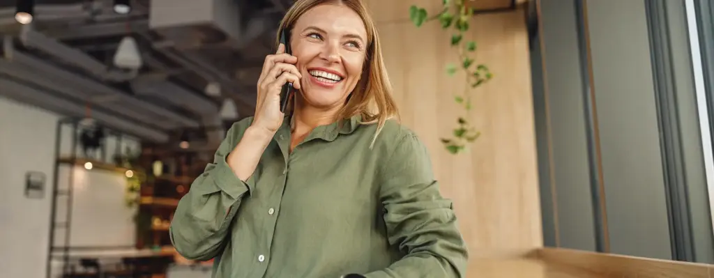 Das Bild zeigt eine lachende Frau, die an einer Theke steht und mit dem Smartphone telefoniert. Das Bild wird im Bereich "Ihr Kontakt" verwendet.