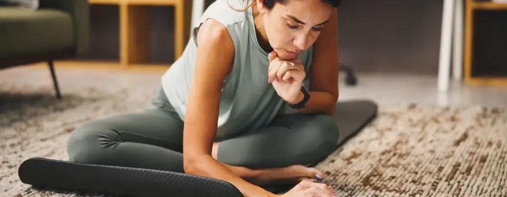 Eine Frau sitzt auf einer Yogamatte im Schneidersitz. Sie ist leicht nach vorne gebeugt und tippt auf ein aufgestelltes Tablet. Das Bild wird im Magazin "Ihr Rücken in Bestform" verwendet.