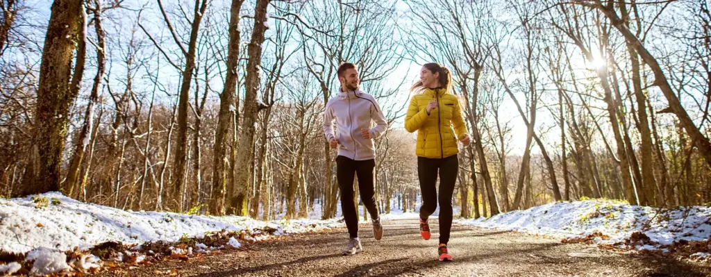 Eine Frau und ein Mann joggen durch einen verschneiten Wald
