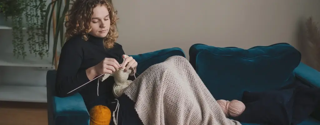 Eine Frau sitzt auf einem Sofa uns strickt
