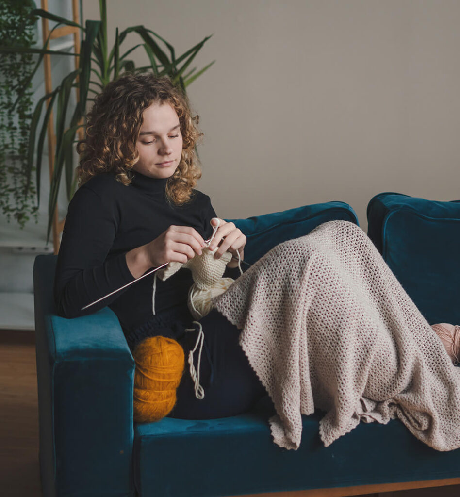 Eine Frau sitzt auf einem Sofa uns strickt