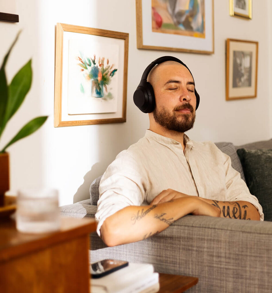 Ein Mann sitzt auf dem Sofa und hört mit geschlossenen Augen Musik mit Kopfhörern