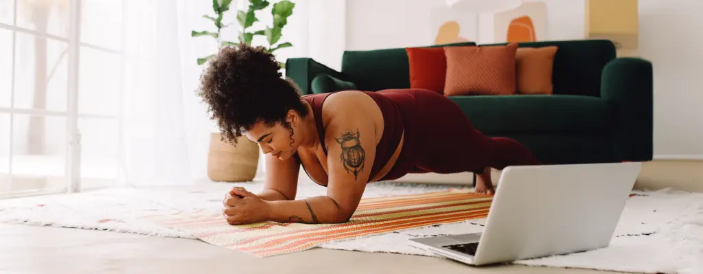 Eine Frau of color macht in einem Gymnastikoutfit eine Plank-Übung