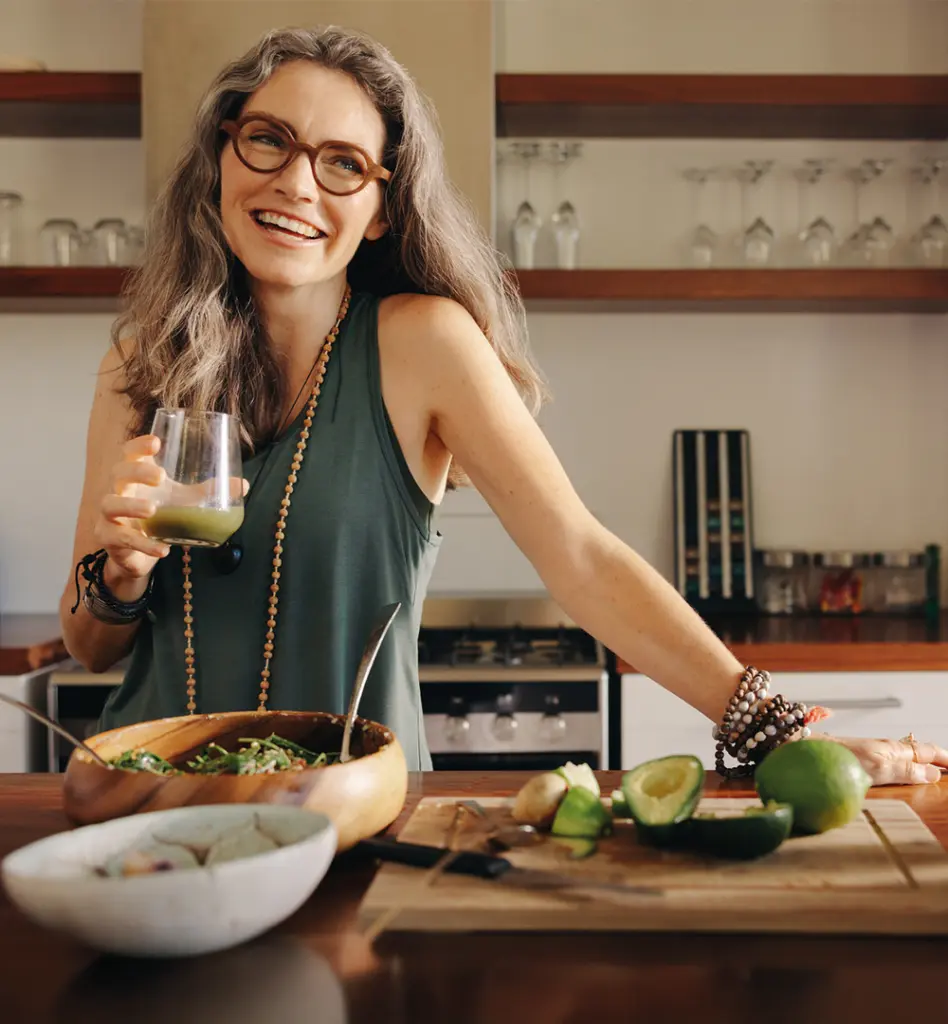 Eine Frau mittleren alters steh lächelnd in der Küche mit einem Glas Saft in der Hand