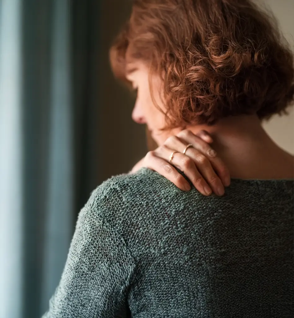 Man sieht eine Frau von hinten wie sie sich an die schmerzende Schulter fasst