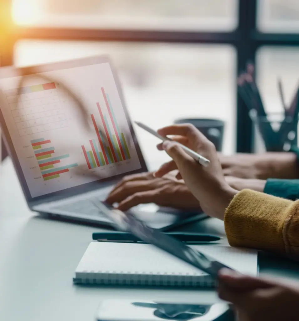 Man sieht einen aufgeklappten Laptop auf einem Schreibtisch in einer Besprechung