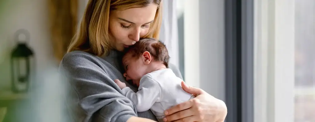 Eine Frau hält ein Baby auf dem Arm und küsst es auf die Stirn.