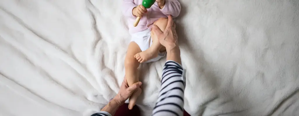 Eine Osteopathin macht mit einem Baby Bewegungsübungen für die Beine