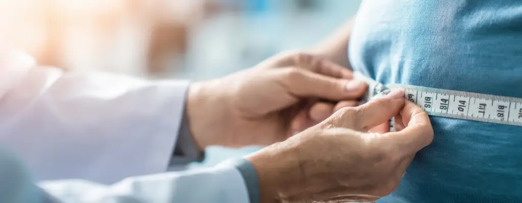 Auf dem Bild vermisst ein Arzt den Bauchumfang seines Patienten mit einem Zentimetermaßband