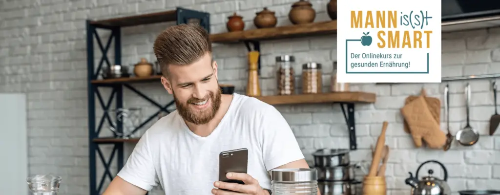 Das Bild zeigt einen Mann der in der Küche sitzt und auf sein Smartphone schaut