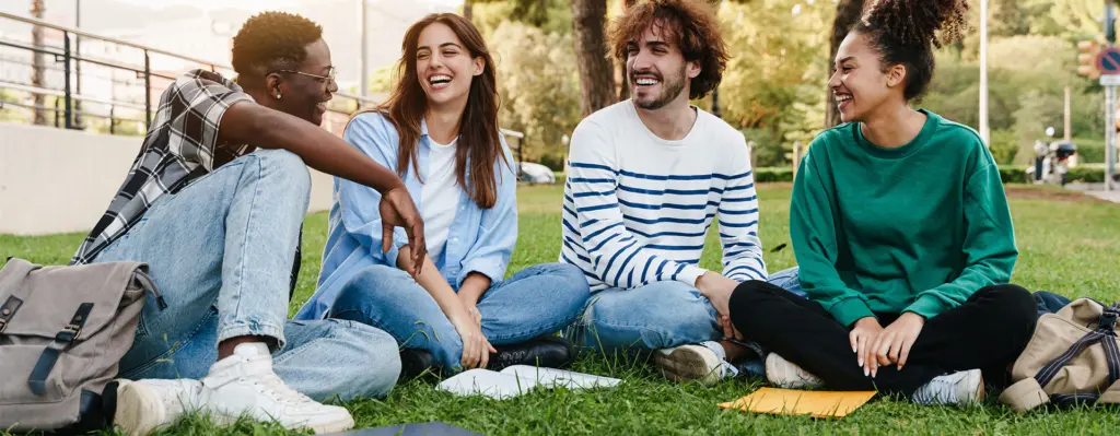 Eine Gruppe junger Leute sitzt auf der Wiese und unterhält sich