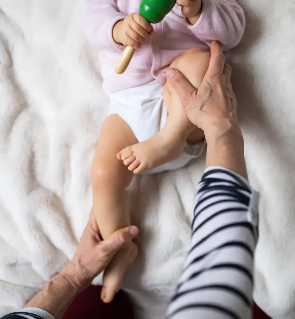 Eine Osteopathin macht mit einem Baby Bewegungsübungen für die Beine
