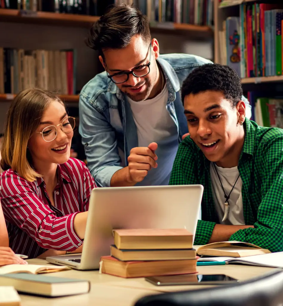 Das Bild zeigt eine Gruppe von Studenten die in einer Bibliothek vor einem Laptop sitzen