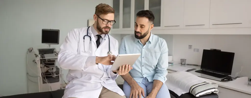 Ein Mann bekommt von einem Arzt seine Werte auf einem Tablet erklärt